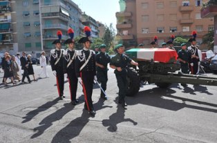 Il feretro posato su di un affusto di cannone e scortato da incursori lascia il luogo della cerimonia. vessilli schierati 